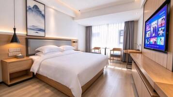 Une chambre d’hôtel moderne dotée d’un grand lit, de tables de chevet, d’un téléviseur à écran plat et d’un coin salon avec une table et des chaises.
