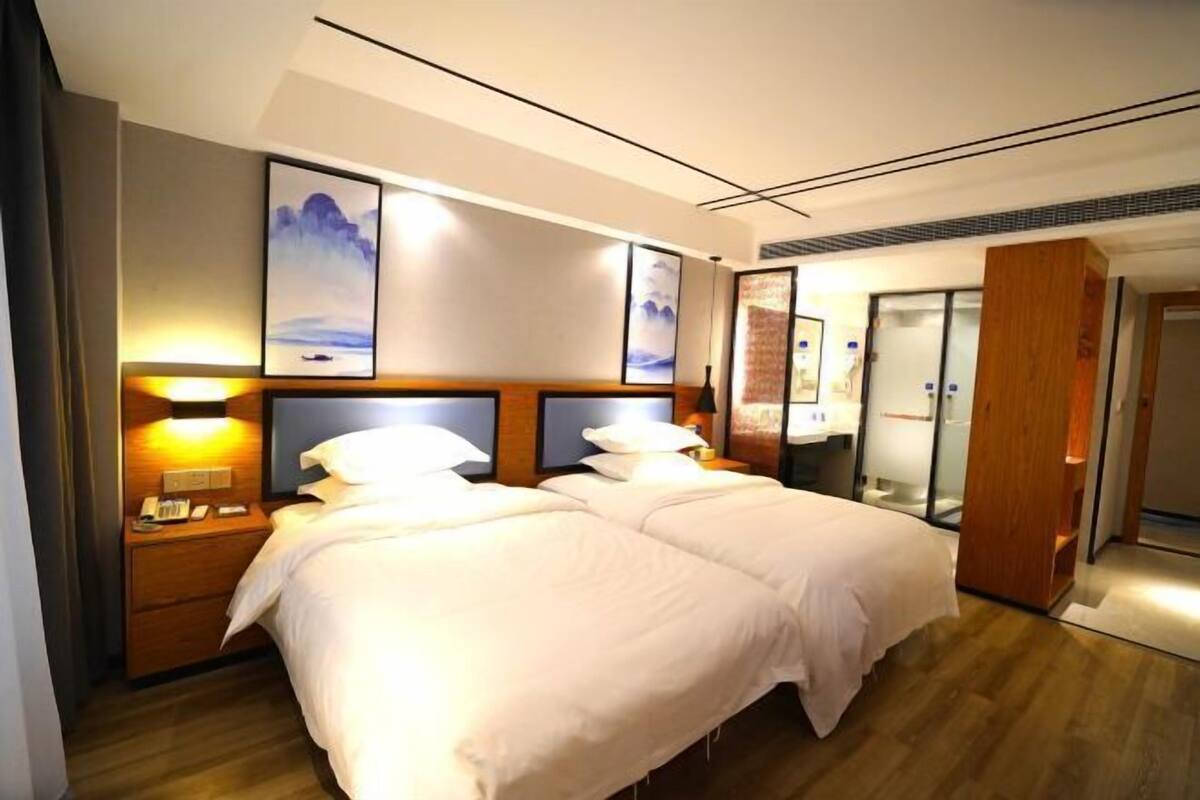 A hotel room with a double bed, bedside tables, a nightstand, a wooden headboard, and framed artwork on the wall.