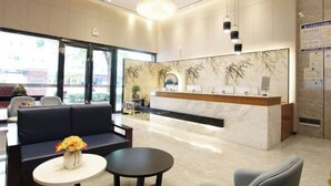 Ein Hotel-Rezeptionsbereich mit Marmor-Theke, einem Kronleuchter, einer Couch und einem kleinen Tisch mit Blumenvase.
