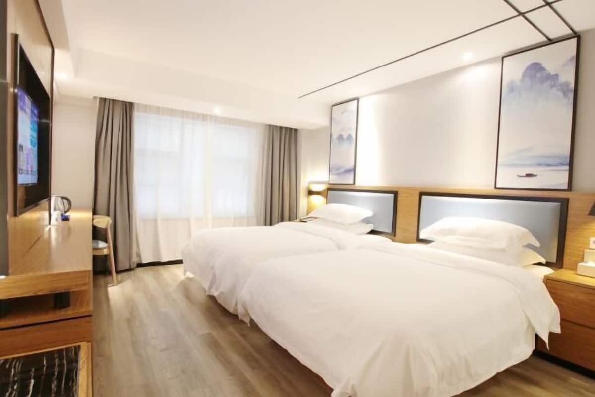 A hotel room with two beds, a TV, a desk, and a window with curtains.