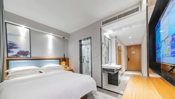 Ein modernes Hotelzimmer mit einem großen Bett, einem Fernseher, einem Schreibtisch und einem Badezimmer mit Glastrennwand.