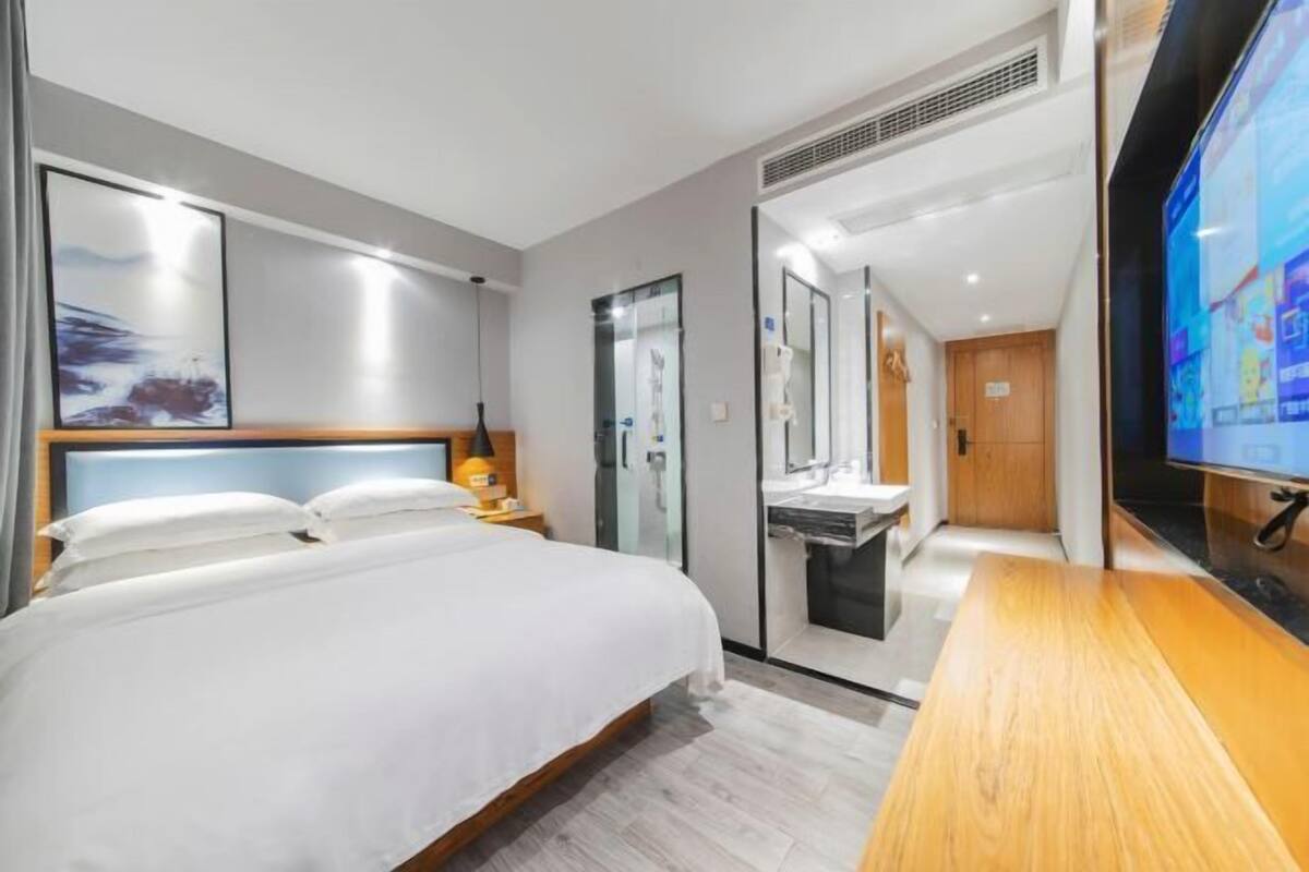 A modern hotel room with a large bed, a TV, a desk, and a bathroom with a glass partition.
