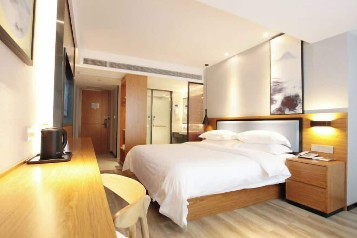 A hotel room with a bed, bedside table, chair, and a desk with a coffee maker.
