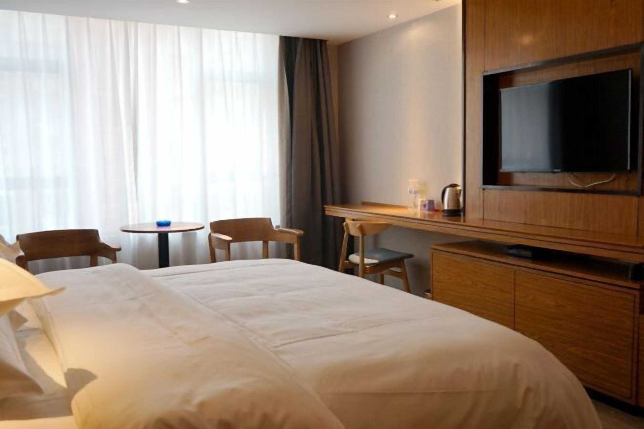 Habitación de hotel con una cama grande, un escritorio, un televisor y una ventana con cortinas.