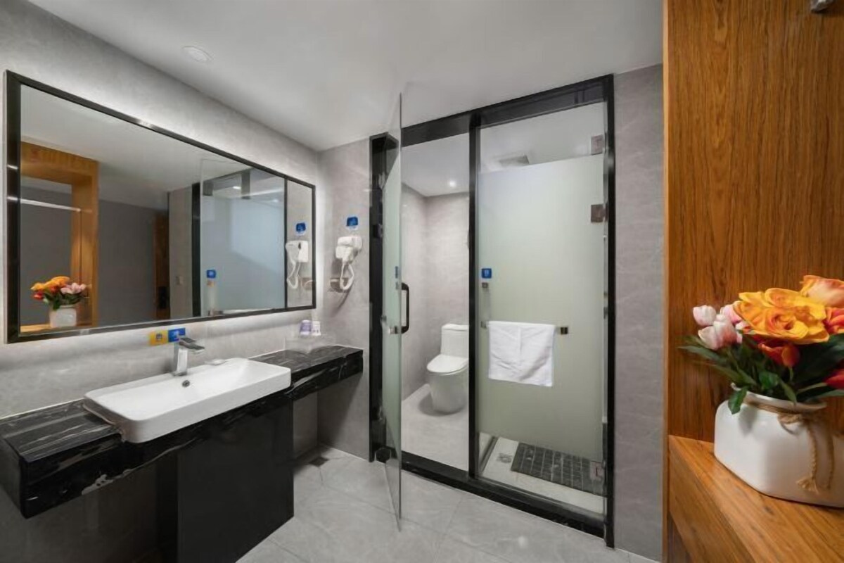 A modern bathroom with a glass shower enclosure, a sink with a mirror, and a toilet visible through the glass.