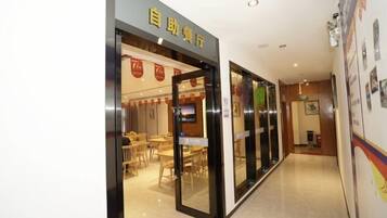 A hotel lobby with a reception desk, a seating area with tables and chairs, and a corridor leading to other parts of the hotel.