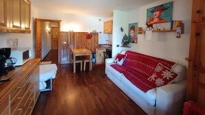 A cozy living room with a sofa, wooden cabinets, and a dining area. - Studio for 4 with terrace, garden and parking (Montgenèvre)