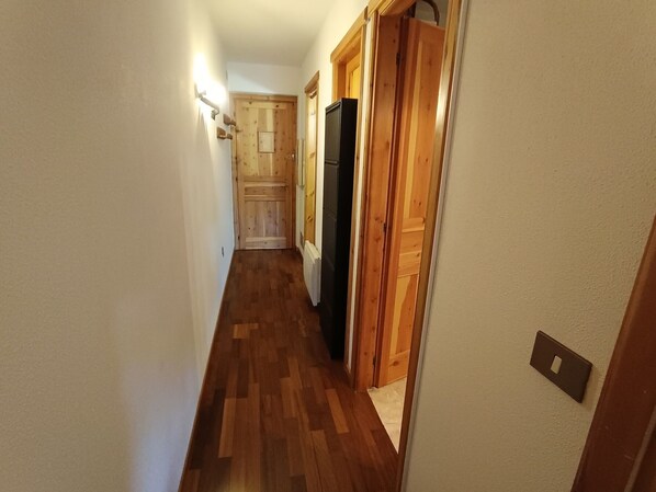 A narrow hallway with wooden flooring and doors leading to different rooms.