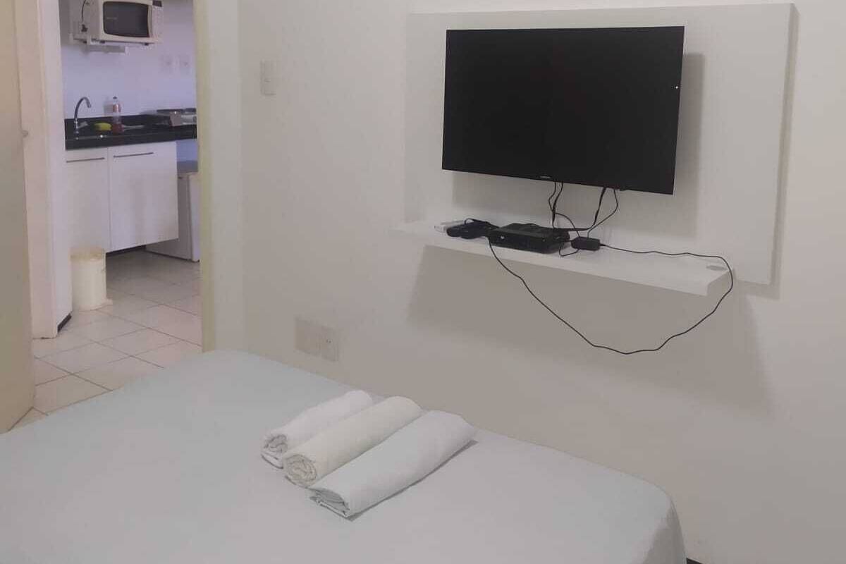 Ett hotellrum med en säng, en platt-TV som är monterad på väggen och ett litet pentry i bakgrunden.