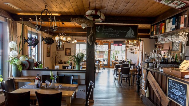 Interior de restaurante con pisos de madera, adornos colgantes y una zona de bar.