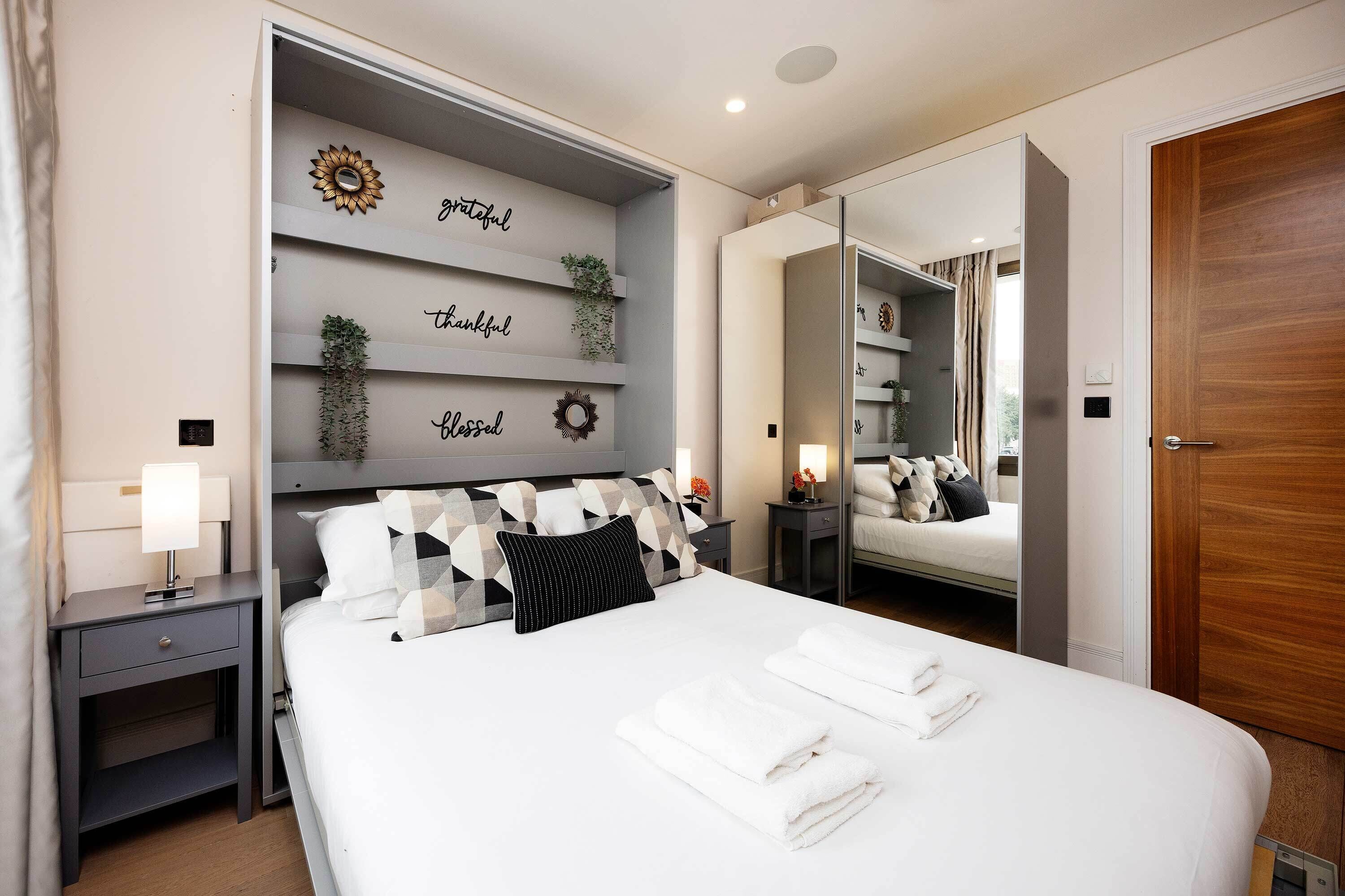 A modern hotel room with a large bed, a nightstand, a mirror, and a wall with decorative items.