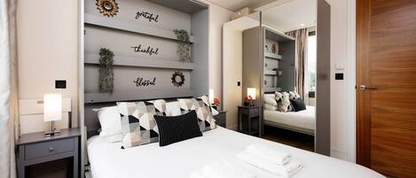 A modern hotel room with a large bed, a nightstand, a mirror, and a wall with decorative items.