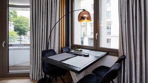 A modern room with a desk, two chairs, a lamp, and a view of buildings through large windows. - Westbourne Curve, by Veeve (London)