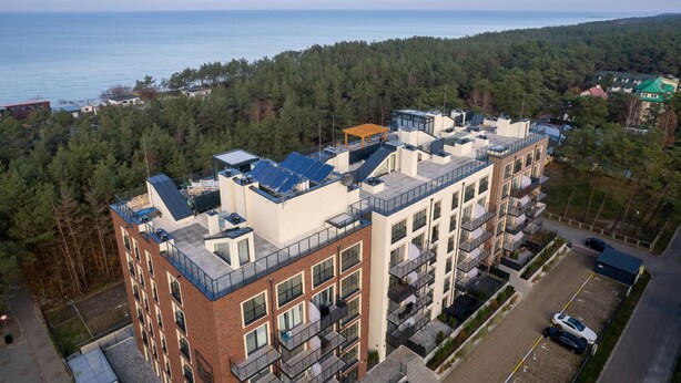 A multi-story building with a rooftop garden, a parking area, and a view of the sea.