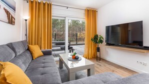 Un soggiorno moderno con un divano grigio, cuscini gialli, un tavolino da caffè in vetro, una TV a schermo piatto e un'ampia finestra con tende gialle.