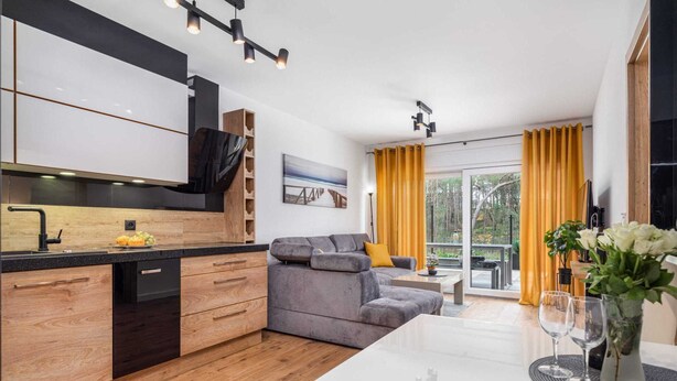 Una cucina moderna con mobili in legno, un divano grigio e un'area pranzo con tavolo bianco e tende gialle.