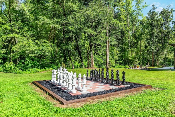 Un tablero de ajedrez situado en un jardín rodeado de árboles.