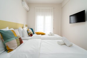 A hotel room with two beds, a flat-screen TV, and a window with sheer curtains.