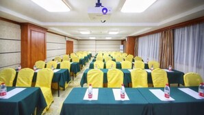 Un salón de conferencias con filas de mesas y sillas, equipado con proyectores y botellas de agua.