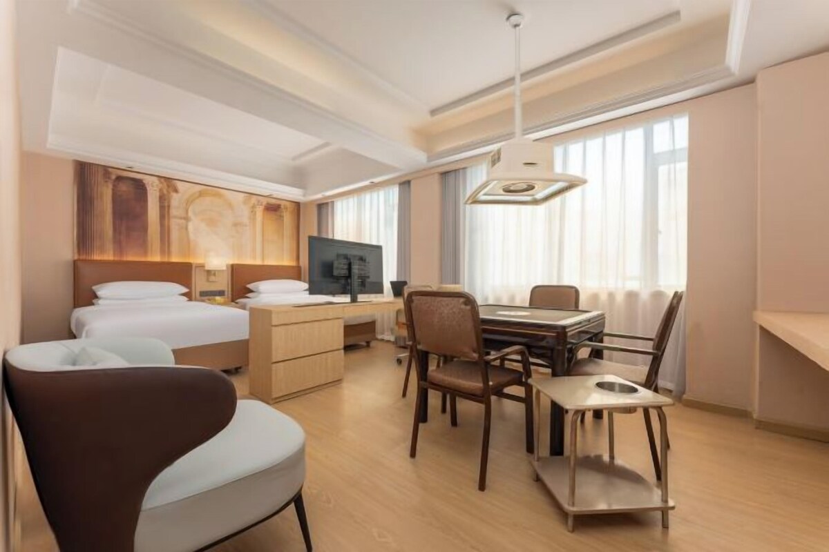 A hotel room with a bed, desk, chairs, and a television.