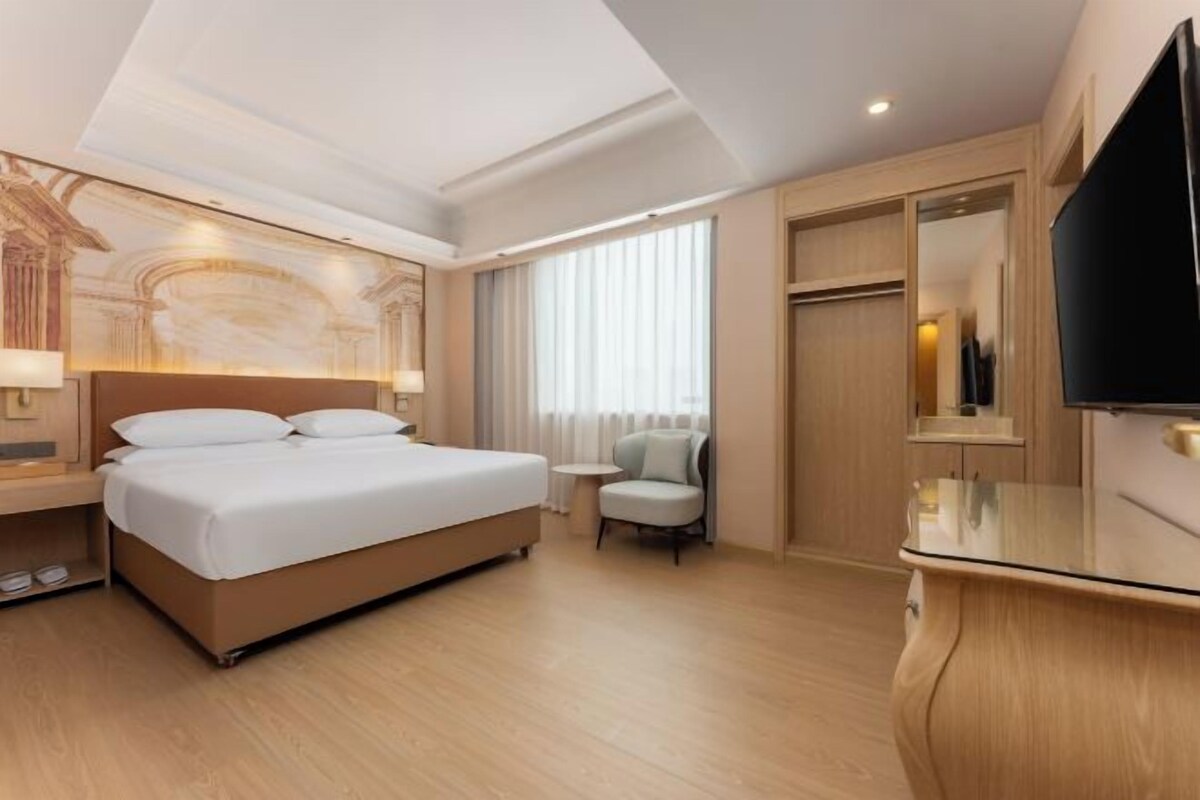 A hotel room with a large bed, a television, a desk, and a chair.