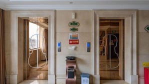 Un hall de hotel con dos ascensores, un cesto de basura y un extintor.