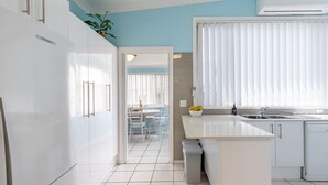 Cocina moderna con armarios blancos, una isla central y un ventanal con persianas.