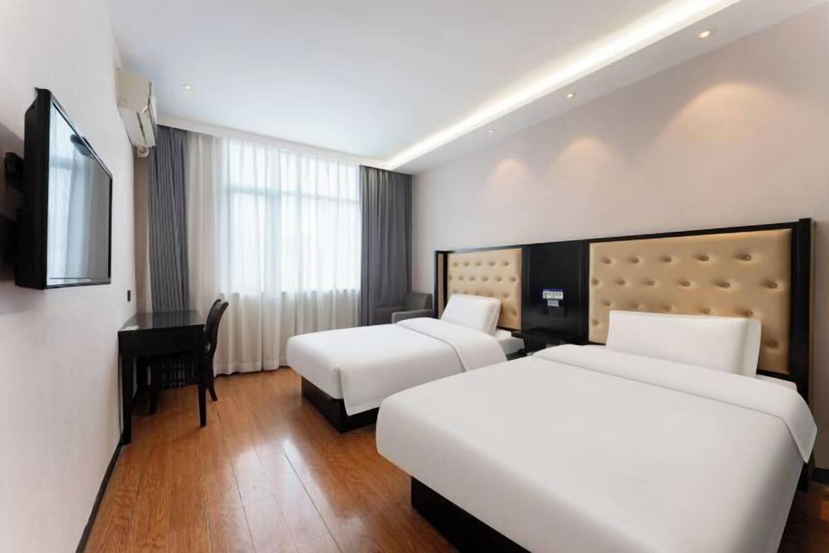 A hotel room with two beds, a desk, a chair, a TV, and a window with curtains.