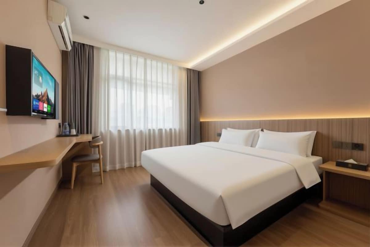 A hotel room with a bed, a desk, a chair, a TV, and a window with curtains.