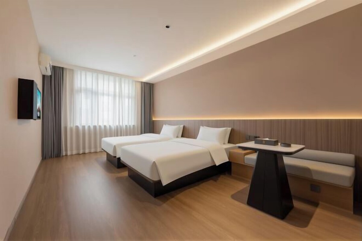 A modern hotel room with two beds, a sofa, a small table, and a TV on the wall.