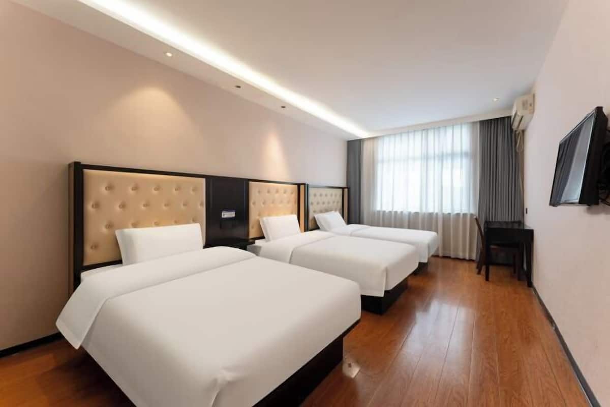 A hotel room with three beds, a flat-screen TV, and a large window with curtains.