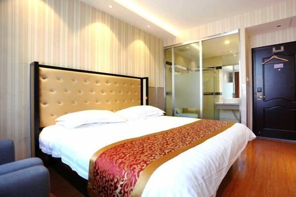 A hotel room with a large bed, a bedside table, a chair, a sliding glass door to the bathroom, and a dark door with a hanger. - Baishang Hotel‌ (Wenzhou)