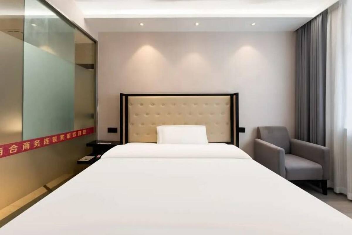 A modern hotel room with a large bed, a chair, a nightstand, and a glass partition with text.