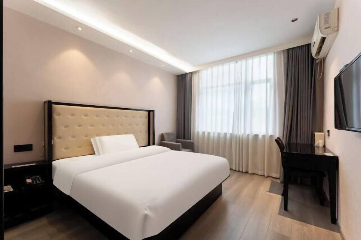 A hotel room with a large bed, a desk, a chair, a TV, and a window with curtains.