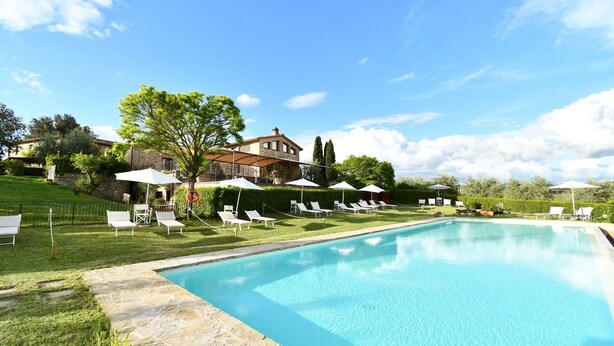 A swimming pool with lounge chairs and umbrellas, surrounded by a stone deck and a grassy area. - Rocche di Valiano, Gelsomino in Siena, pool use, AC (Castelnuovo Berardenga)