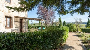 A stone building with a covered patio, a garden path, and a view of the countryside. - Rocche di Valiano, Gelsomino in Siena, pool use, AC (Castelnuovo Berardenga)