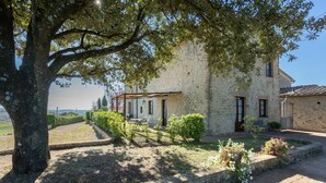 A stone building with a covered outdoor seating area, surrounded by greenery and a tree. - Rocche di Valiano, Gelsomino in Siena, pool use, AC (Castelnuovo Berardenga)