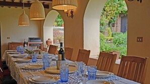 Un espace repas avec une longue table dressée pour un repas, agrémenté de verres et d’assiettes bleus, de chaises en bois et de lampes en osier suspendues.