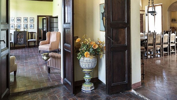 Une pièce spacieuse avec une grande porte en bois, un coin repas avec plusieurs chaises et un vase décoratif rempli de fleurs.