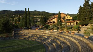 Ein steiner Amphitheater mit gestuften Sitzreihen, umgeben von angelegten Gärten und einer Hügelkulisse.