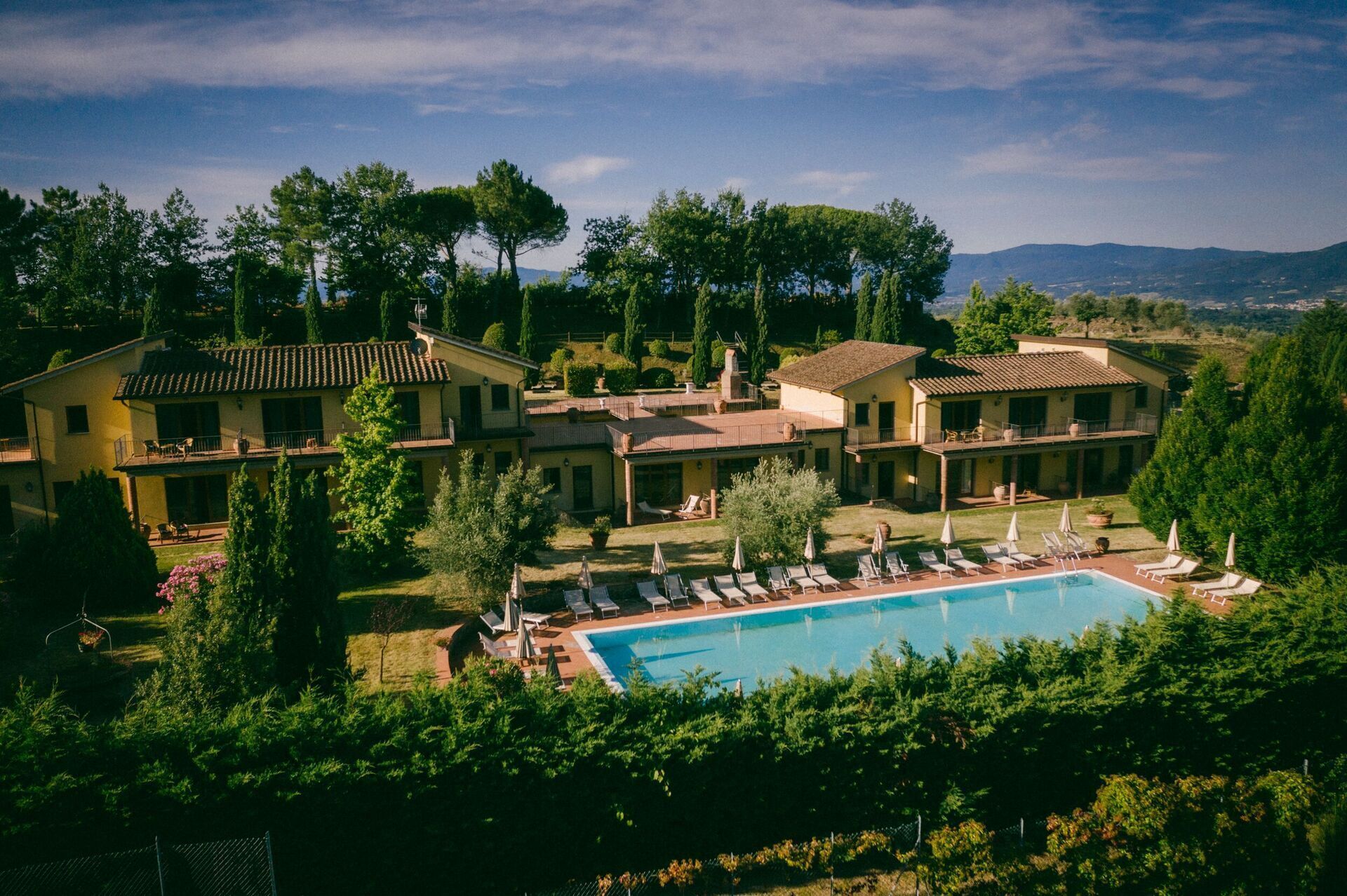 Eine großzügige Villa mit Swimmingpool, mehreren Balkonen und üppiger Bepflanzung.