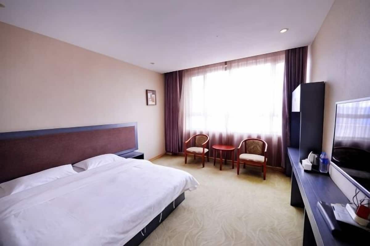 Une chambre d’hôtel avec un lit, un bureau avec une télévision, deux chaises et une fenêtre avec des rideaux.