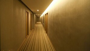 Ein Hotelgang mit Teppichboden, rechts und links Türen und einer Lichtquelle.