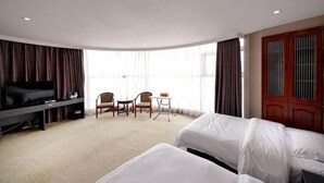 Ein Hotelzimmer mit Fernseher, zwei Betten, einem Schreibtisch, Stühlen und einem großen Fenster.