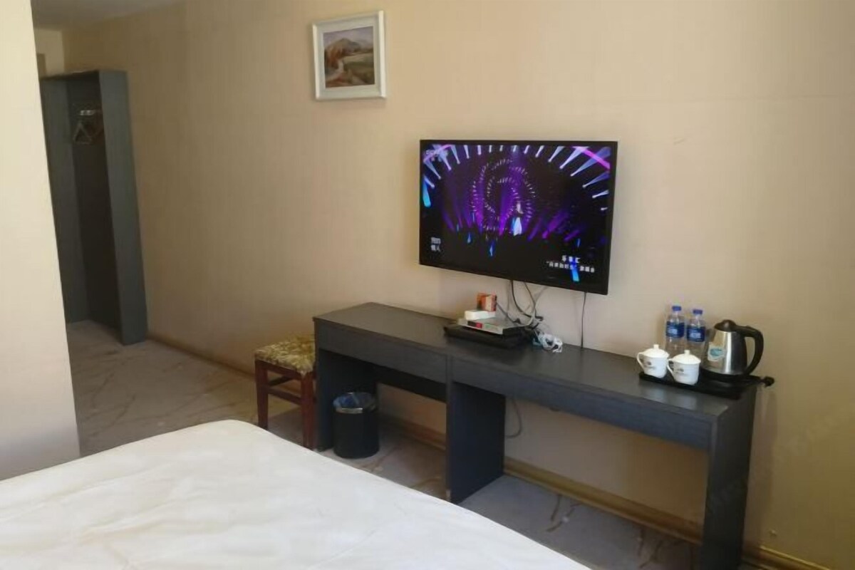 Ein Hotelzimmer mit Bett, Schreibtisch, Flachbildfernseher, Stuhl, Mülleimer und Kaffeemaschine.