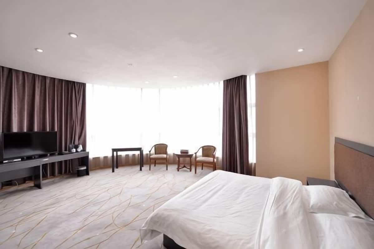 Une chambre d’hôtel avec un lit, une télévision, un bureau, deux chaises et une grande fenêtre.