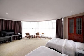 A hotel room with a TV, two beds, a desk, and a chair.