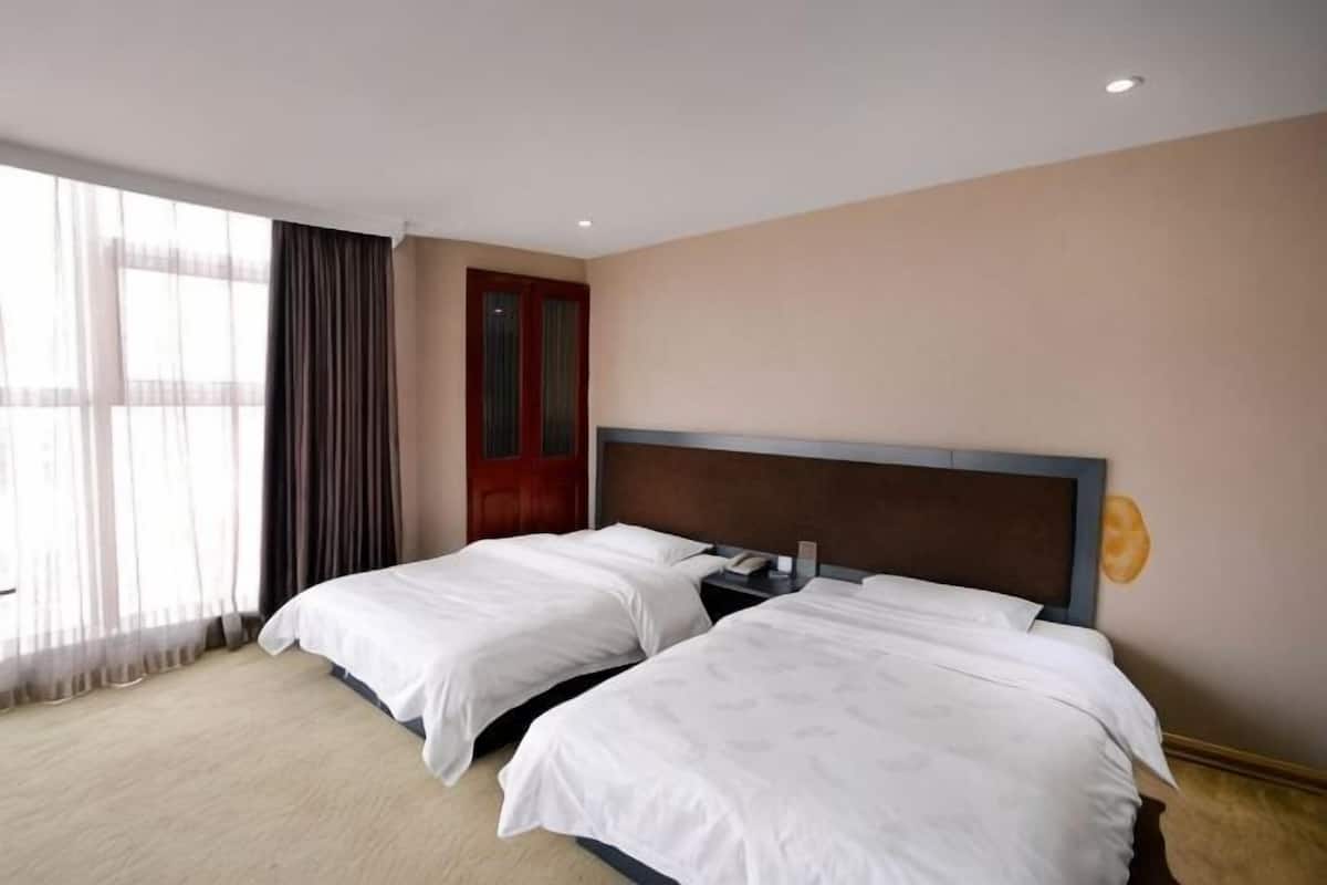 Une chambre d’hôtel avec deux lits, une porte en bois et une grande fenêtre avec des rideaux.