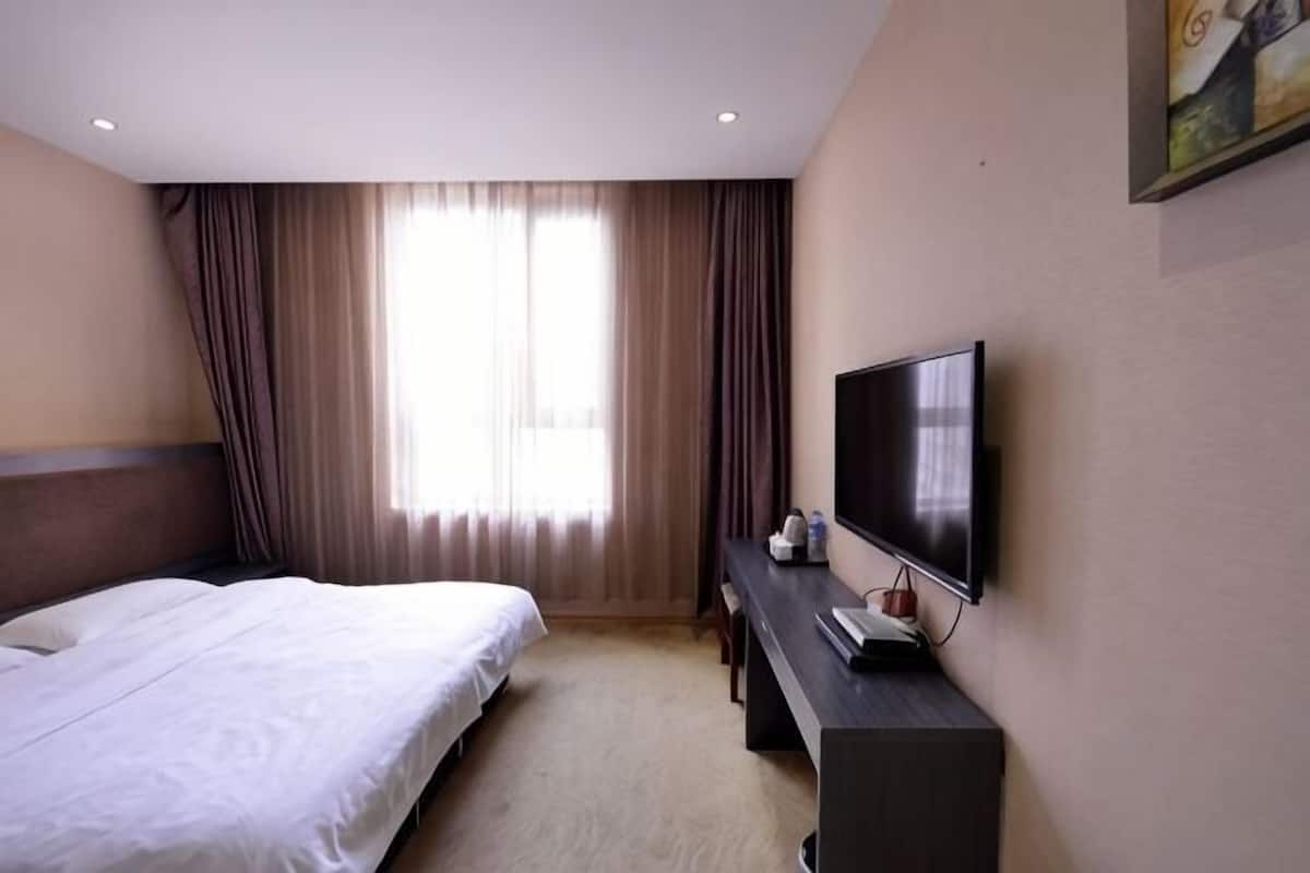 Une chambre d’hôtel avec un lit, un bureau doté d’un téléviseur à écran plat et une fenêtre avec des rideaux.