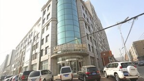 Ein mehrstöckiges Hotel mit geschwungener Fassade, einer markanten Eingangspforte und mehreren parkenden Autos davor.